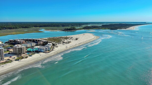 Vista aérea de una zona costera con edificios a lo largo de la orilla, una playa y un río o bahía.