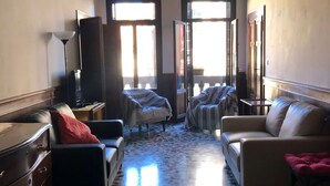 A spacious living room with a large chandelier, a sofa, a chair, and a coffee table. There are two windows allowing natural light to enter. - VENICE SANCTUARY: 4-BEDROOM APARTMENT, CENTRAL, CANAL VIEWS WITH 2 TERRACE  (Venezia)