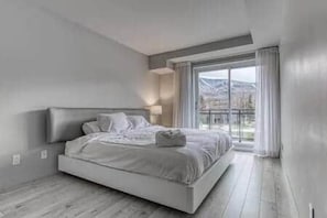 Quarto moderno com cama grande, mesa de cabeceira e janela com vista para o exterior.