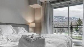 Habitació d'hotel amb un llit gran, vistes a les muntanyes per la finestra i una làmpada a la nit.