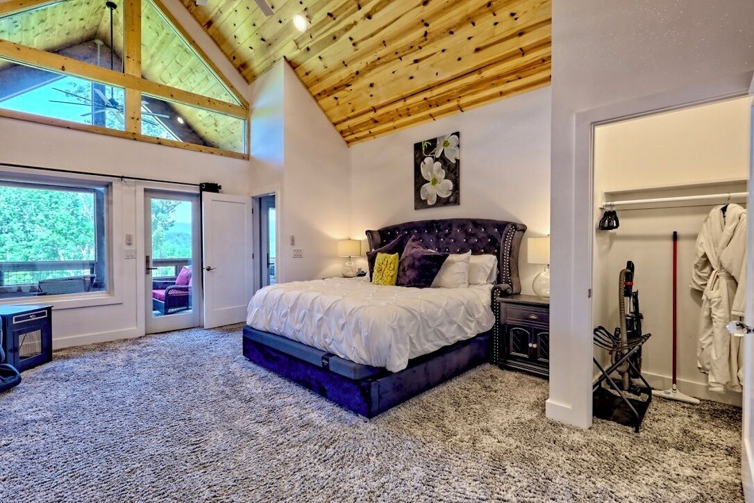 A bedroom with a large bed, a wooden ceiling, a painting, and a view through a door.