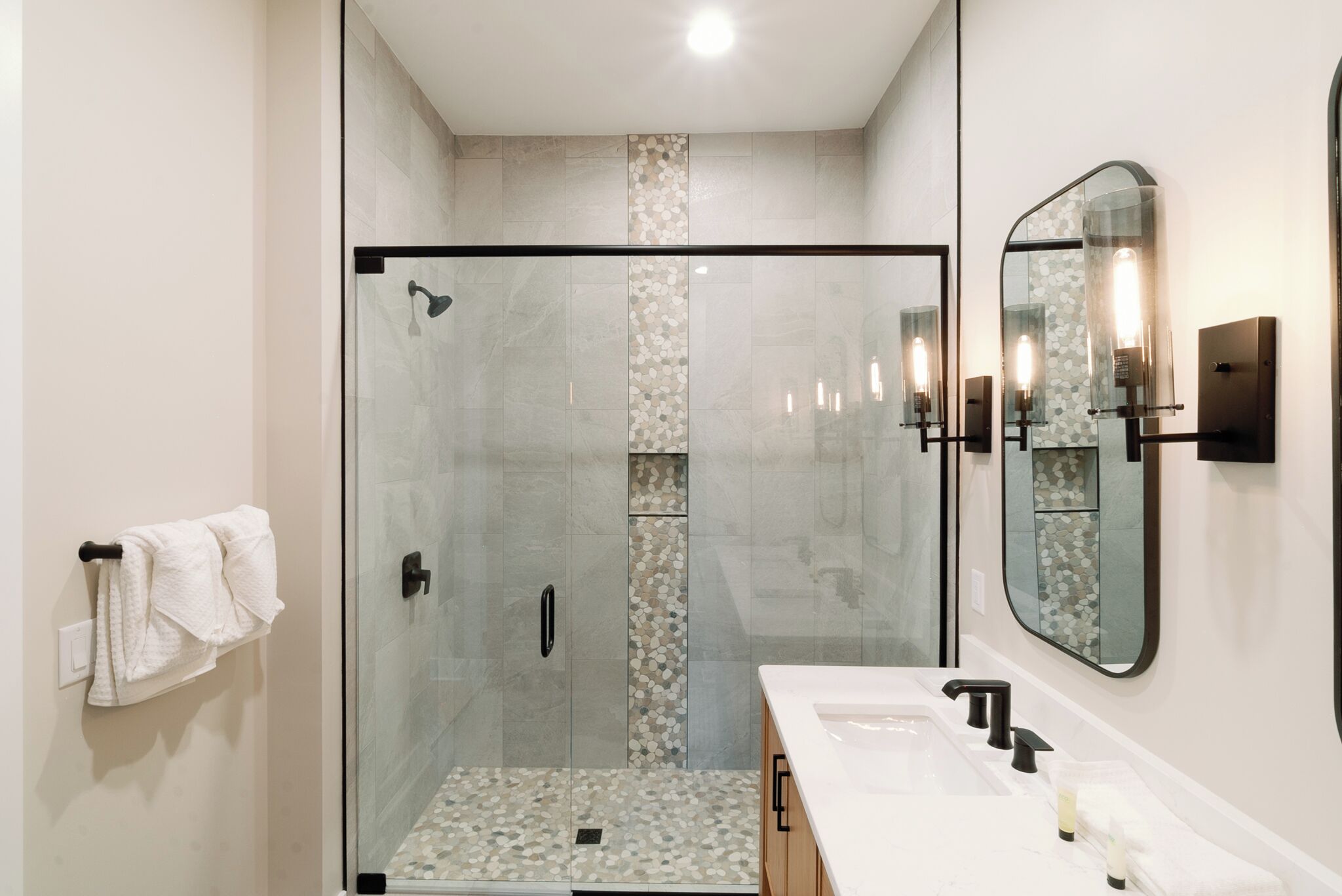 Un baño moderno con cabina de ducha de vidrio, un espejo grande y una encimera blanca con lavabo.