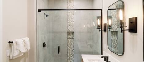Un baño moderno con cabina de ducha de vidrio, un espejo grande y una encimera blanca con lavabo.