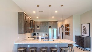 A modern kitchen with a large island, bar stools, pendant lighting, and stainless steel appliances.