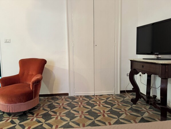 A room with a closed wardrobe, a television on a wooden stand, and a patterned floor.
