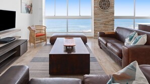 Una sala de estar con un ventanal grande, un televisor de pantalla plana, una mesa de centro de madera y un sofá de cuero marrón.