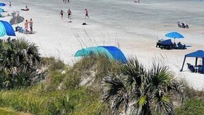Ein Strand mit einer Mole, Zelten und Menschen.