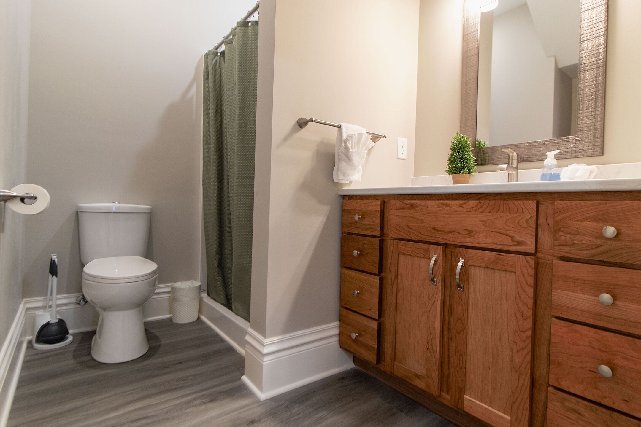 A bathroom with a toilet, shower curtain, wooden vanity, and a mirror.
