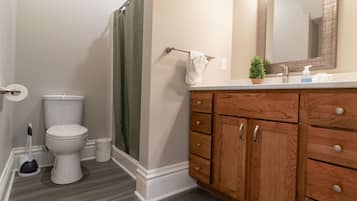 A bathroom with a toilet, shower curtain, wooden vanity, and a mirror.