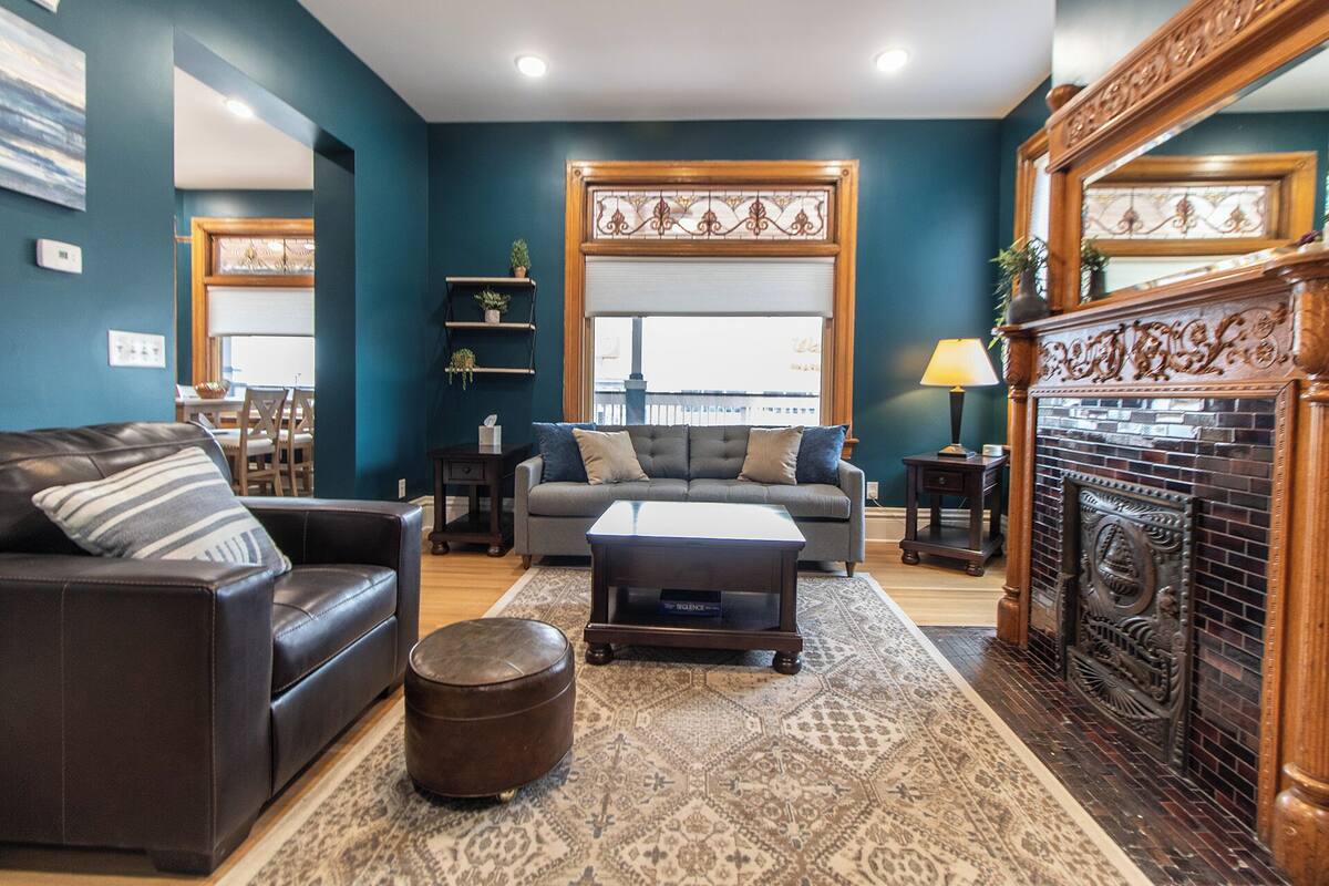 A living room with a sofa, armchair, ottoman, and a fireplace.