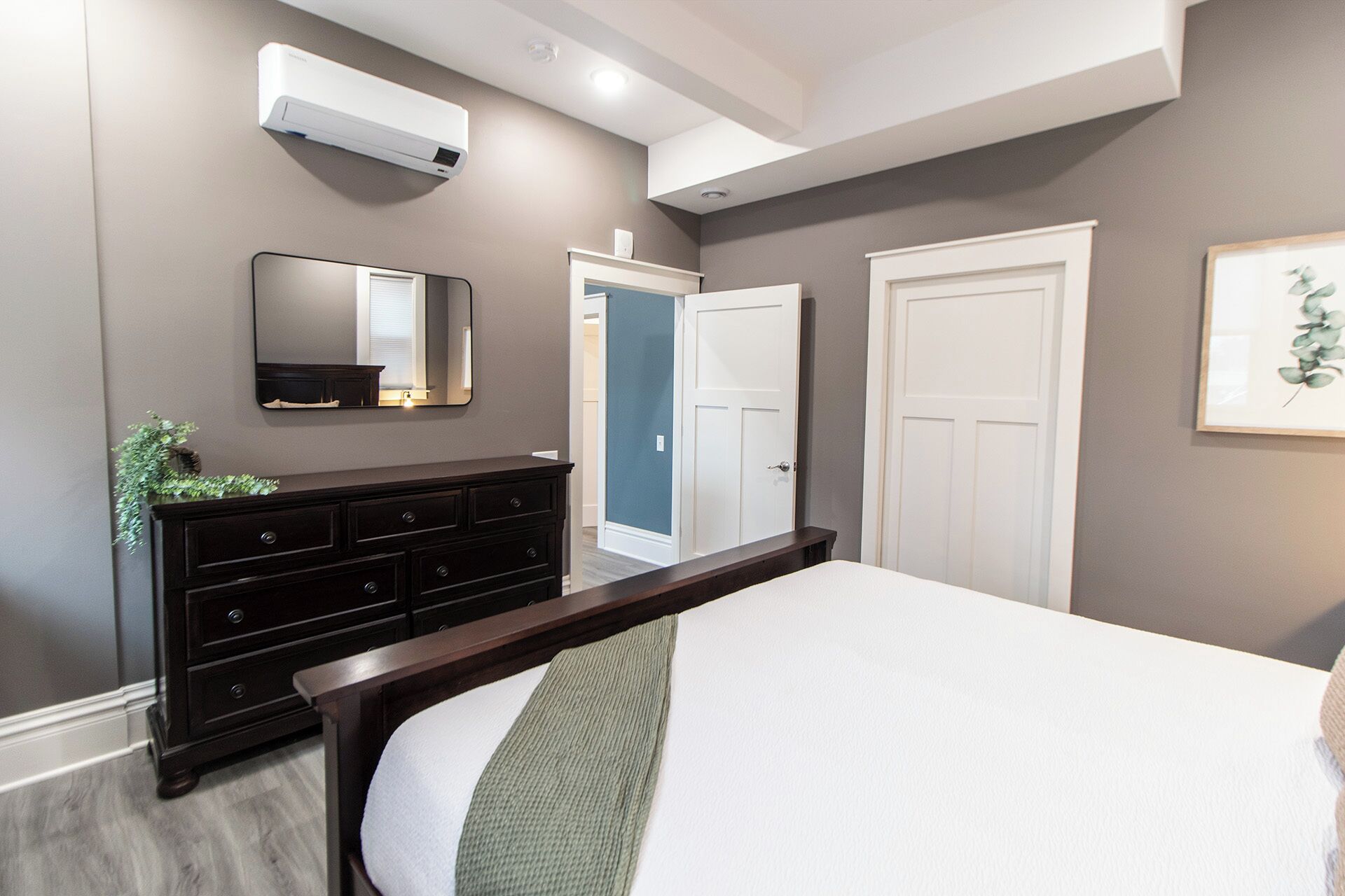 A bedroom with a bed, dresser, mirror, and white doors.