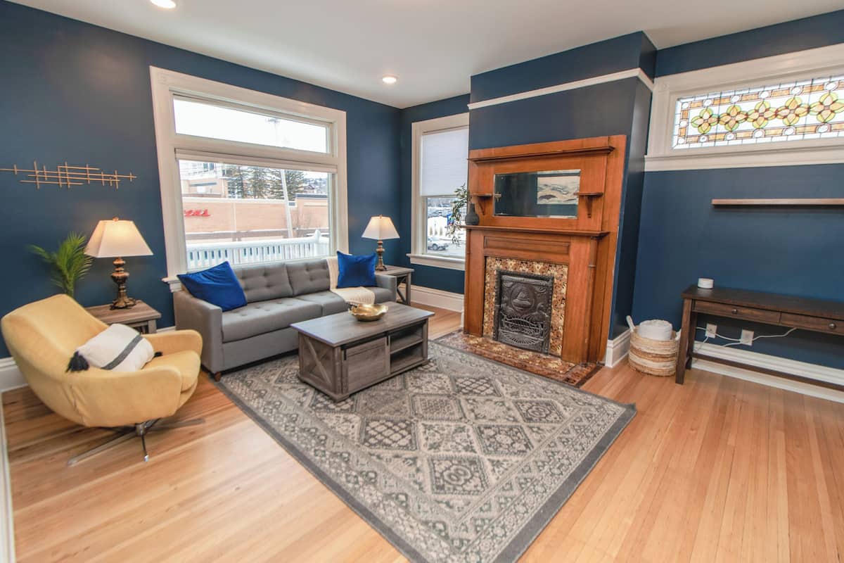 A living room with a sofa, armchair, coffee table, fireplace, and large windows.