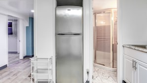A modern kitchen with white cabinets, a stainless steel refrigerator, and a marble-tiled floor.
