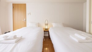 Habitación de hotel con dos camas, una puerta de madera, una mesita de noche con lámpara y toallas sobre las camas.