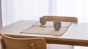 Una mesa de madera con dos tazas de cerámica sobre individuales.