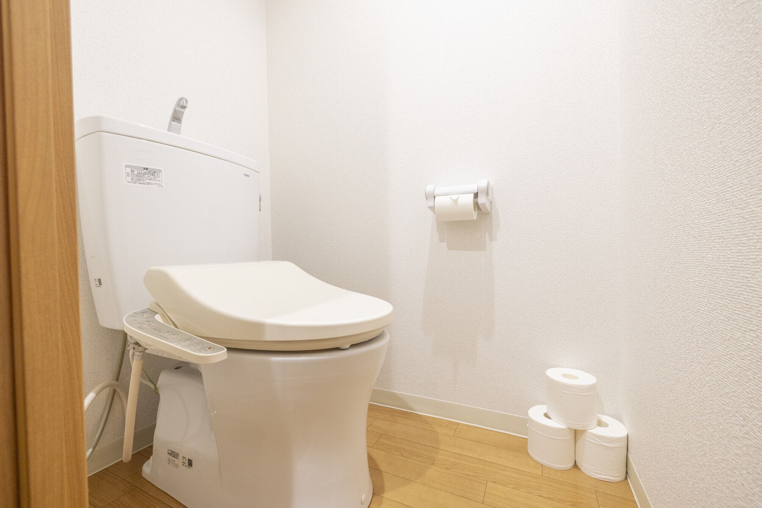 A white toilet with a control panel, a toilet paper holder, and three rolls of toilet paper on the floor.