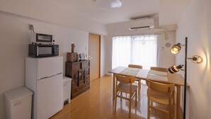 Cocina compacta con microondas, refrigerador y armarios de madera. Cuenta con un comedor con mesa y sillas, y una lámpara en el techo.