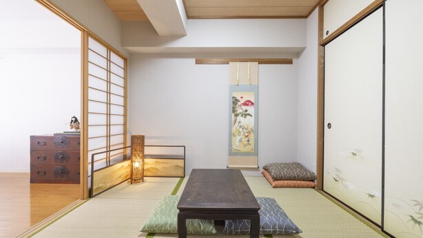 Una habitación tradicional japonesa con suelo de tatami, una mesa de madera baja, cojines, una puerta corredera y un biombo decorativo.