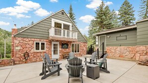 A two-story house with a stone facade, a balcony, and outdoor seating with Adirondack chairs. - Private Family Home: Spacious Patio, Hot Tub, Fire Pit by Forest & Peak Retreats (Cascade-Chipita Park)