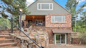 A two-story house with a stone facade, a balcony, and a staircase leading to the entrance. - Private Family Home: Spacious Patio, Hot Tub, Fire Pit by Forest & Peak Retreats (Cascade-Chipita Park)