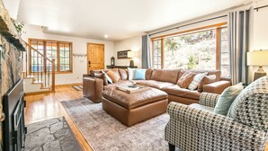 A spacious living room with a large sectional sofa, a patterned armchair, and a wooden staircase. - Private Family Home: Spacious Patio, Hot Tub, Fire Pit by Forest & Peak Retreats (Cascade-Chipita Park)
