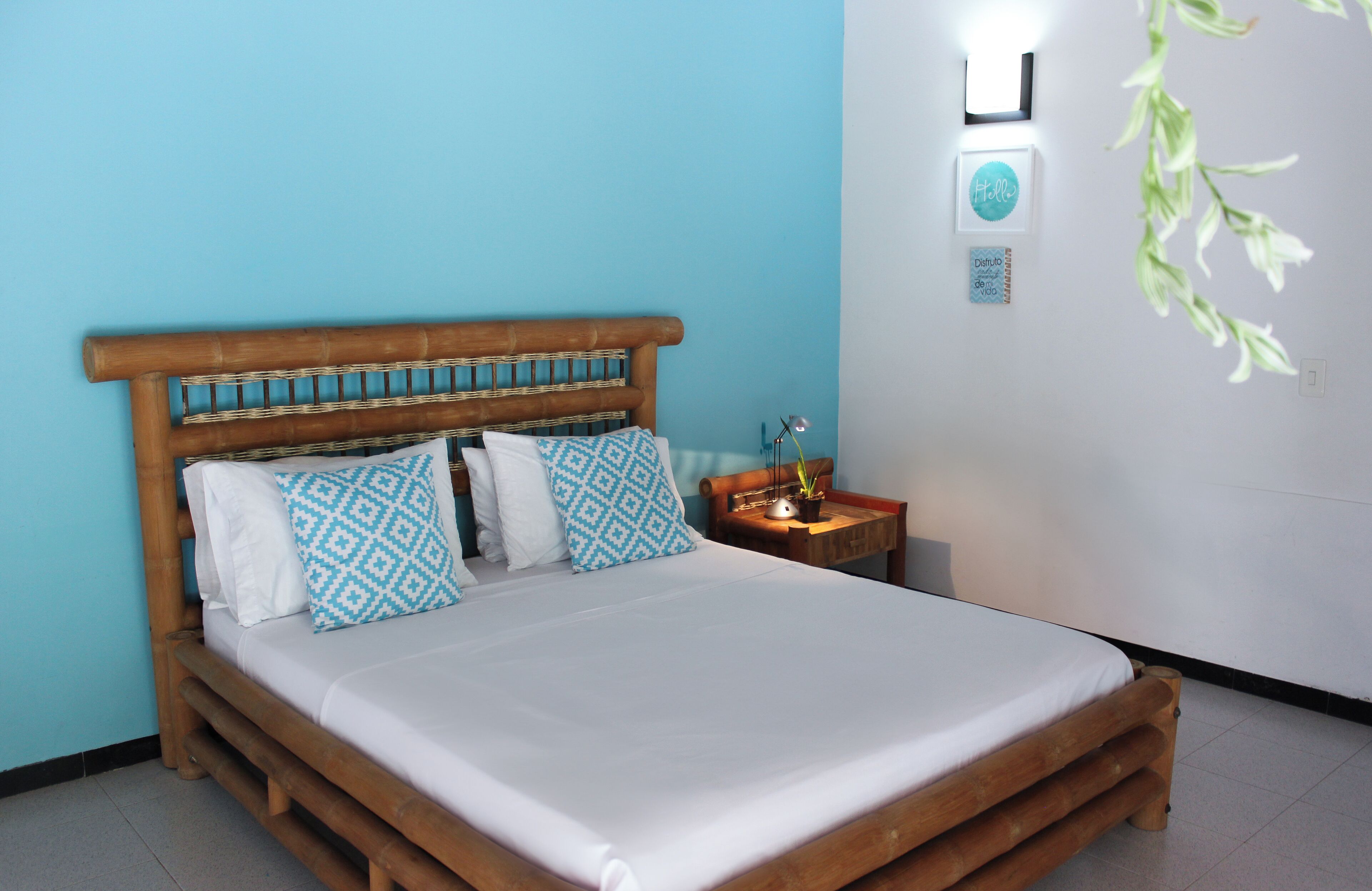 A bed with a wooden headboard, two pillows, a bedside table with a lamp, and a wall-mounted light fixture.