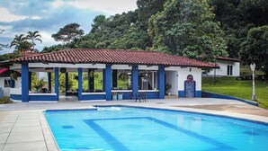 A swimming pool with a tiled deck, a covered seating area, and a building with a red-tiled roof. - Hacienda siete sentidos  (La Mesa)