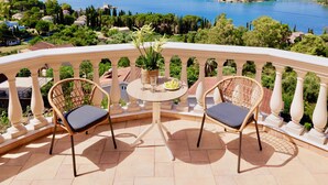 Un balcon avec deux fauteuils en osier et une petite table, d’où l’on peut admirer un lac et le paysage environnant.