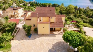 Une maison à deux étages, avec un toit en tuiles, entourée de verdure et offrant une vue sur un lac.