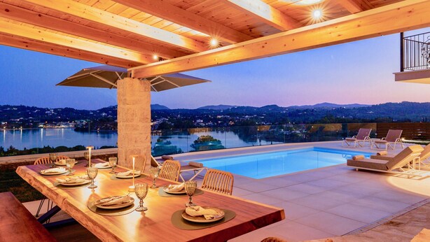 Un coin repas avec une table dressée pour six personnes, donnant sur une piscine et offrant une vue pittoresque sur un lac au crépuscule.
