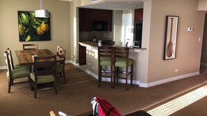 A dining area with a wooden table and chairs, a kitchen with a microwave and refrigerator, and a painting on the wall. - Hilton Hawaiian Village Lagoon Tower 2BR 2BA sleeps 6 (Honolulu)