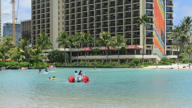 A resort with a large building, palm trees, and a clear blue pool with people in watercraft. - Hilton Hawaiian Village Lagoon Tower 2BR 2BA sleeps 6 (Honolulu)