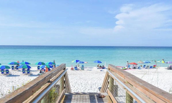 A beach with a wooden walkway leading to the shore, beach chairs, and umbrellas. - Coastal Charm, CANAL FRONT 🌴Condo, 5 Pools, Hot Tub, walk to beach Dog-Friendly! (Destin)
