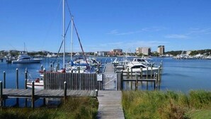 Un port de plaisance où sont amarrés de nombreux bateaux, une passerelle en bois menant aux quais et des bâtiments en arrière-plan.