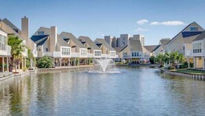 Un quartier résidentiel avec des maisons modernes, une fontaine centrale et un plan d’eau paisible.
