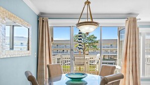 Un coin repas avec une table et des chaises en verre, un luminaire suspendu et une vue sur un balcon aménagé avec du mobilier d’extérieur.