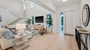 A spacious living area with a staircase, a flat-screen TV, a sofa, a coffee table, and a side table with a lamp. - Brand new 4bdr, 5 bath luxury house 1 mile from 5th Avenue and Beached (Naples)