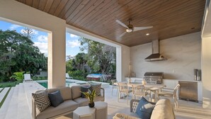 An outdoor patio with a sofa, chairs, a dining table, and a grill area. - Brand new 4bdr, 5 bath luxury house 1 mile from 5th Avenue and Beached (Naples)