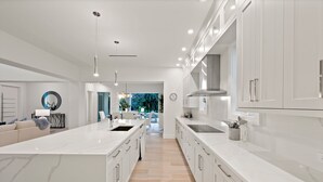 A modern kitchen with white cabinetry, a large island, and a view into the dining area. - Brand new 4bdr, 5 bath luxury house 1 mile from 5th Avenue and Beached (Naples)
