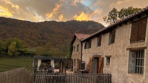 A pool area with a wooden deck, a stone building with wooden shutters, and a mountainous backdrop. - Enjoy nature in its purest form (Vallfogona de Ripollès)