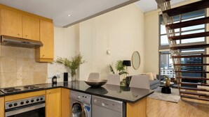 A modern kitchen with built-in appliances, a washing machine, and a dining area with a view of the city. - Elegant 1 Bedroom Loft - Soho on Rose (Cape Town)