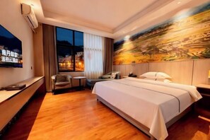 A hotel room with a large bed, a desk with a chair, a small table, and a TV on the wall.