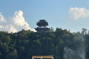 A traditional building with a multi-tiered roof, surrounded by dense forest. - Nandan Home Inn Paibaiyun Hotel (Nandan)