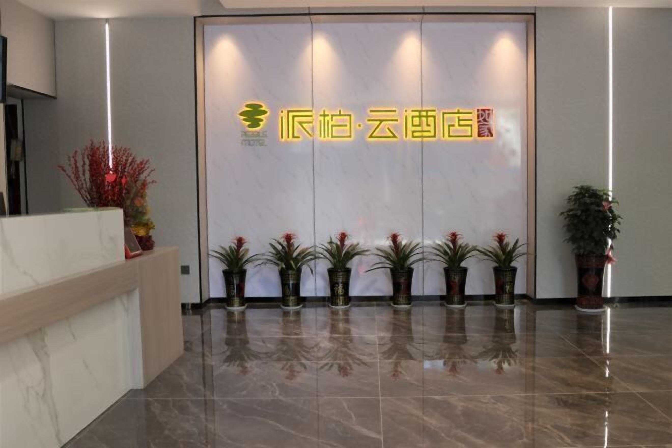 A hotel reception area with a modern design, featuring a reception desk, a series of potted plants, and a prominent hotel sign.