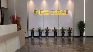 A hotel reception area with a modern design, featuring a reception desk, a series of potted plants, and a prominent hotel sign.