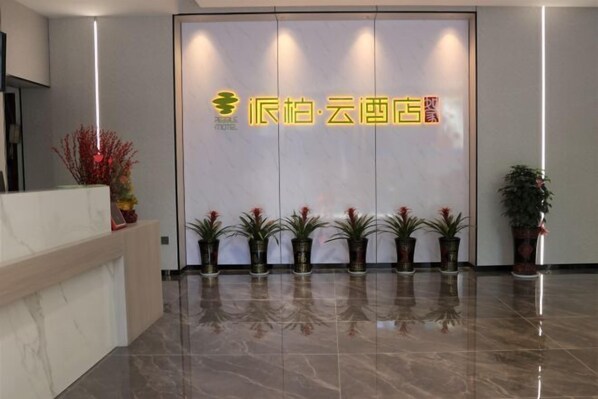 A hotel reception area with a modern design, featuring a reception desk, a series of potted plants, and a prominent hotel sign. - Nandan Home Inn Paibaiyun Hotel (Nandan)