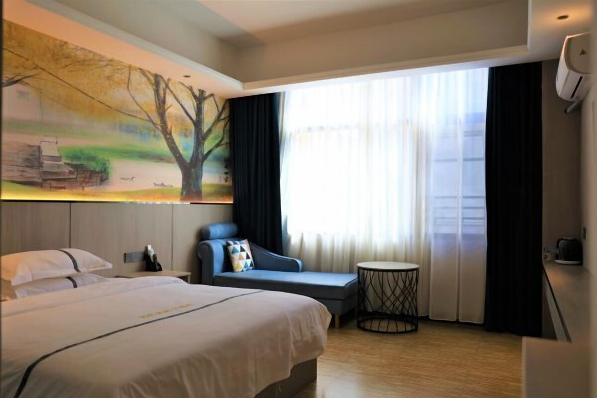 A hotel room with a large bed, a seating area with a view of the city, and a painting on the wall.