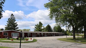 A motel with a red exterior, multiple rooms, a parking lot, and surrounding greenery. - Bonne Belle Motel (Kewaskum)