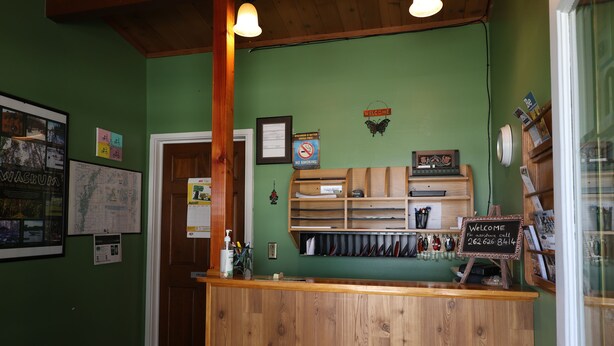 A reception area with a wooden counter, a welcome sign, a no smoking sign, and various items on shelves. - Bonne Belle Motel (Kewaskum)