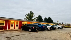 A row of RVs parked in a lot with a red building in the background. - Bonne Belle Motel (Kewaskum)